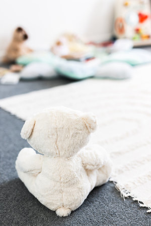 white teddy bear seen from behind in beautiful happy and messy nursery or children's room with colorful wooden toys and soft pillows and rugs, childhood learning and home decor conceptsの写真素材