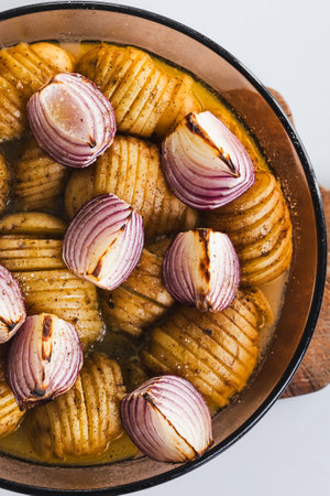 plant-based roasted hasselback potatoes with onions in round oven tray, healthy vegan food recipesの写真素材