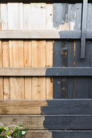 half painted backyard retaining wall or fence, charcoal vs bare wood, home improvement and renovation conceptの写真素材