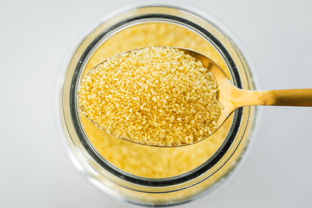 pantry staple close-up, spoonful of cous cous over clear glass jar shot from above, daily...