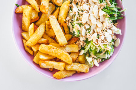 plate with half chips and half salad topped with tofu and almonds, healthy food vs junk food concept...