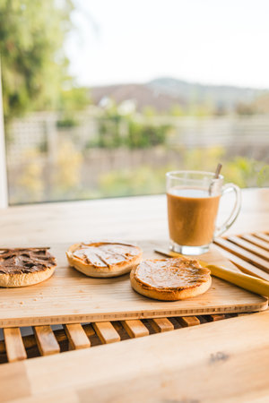 peanut butter and chocolate English muffins with coffee mug on breakfast table with backyard bokeh,...