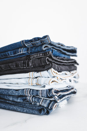 pile of jeans in different color denim fabric neatly folded and piled up on minimalistic backgroundの写真素材