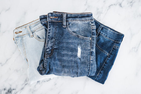 pile of jeans in different color denim fabric neatly folded and piled up on minimalistic background
