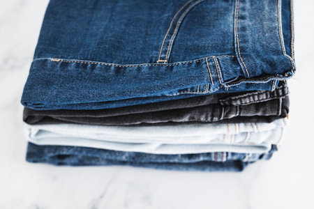 pile of jeans in different color denim fabric neatly folded and piled up on minimalistic backgroundの写真素材
