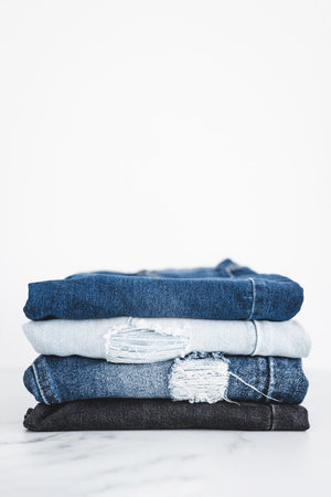 pile of jeans in different color denim fabric neatly folded and piled up on minimalistic background
