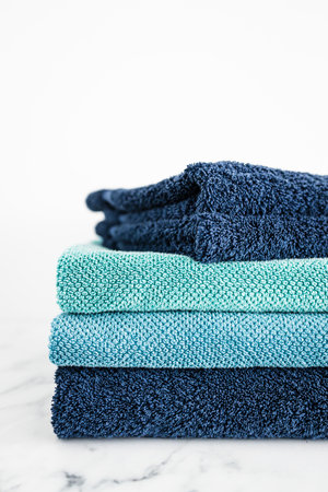 pile of bath towels, neatly folded, blue and teal color, on minimalistic white marble background, household and daily items conceptの写真素材