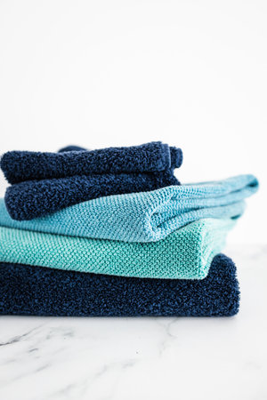 pile of bath towels, neatly folded, blue and teal color, on minimalistic white marble background, household and daily items conceptの写真素材