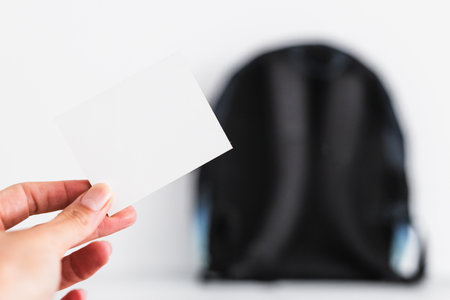 hand holding blank message label in front of backpack bokeh, concept of backpacking, travelling or going to schoolの写真素材