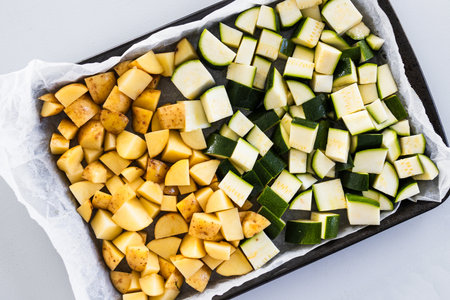 chopped baby potatoes and zucchini in small cubes on an oven tray, prepared for roasting in a simple homemade dishの写真素材