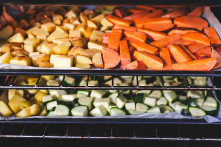 oven with trays of cubed baby potatoes, sweet potatoes and zucchini, meal prep healthy ingredients for homemade mealsの写真素材