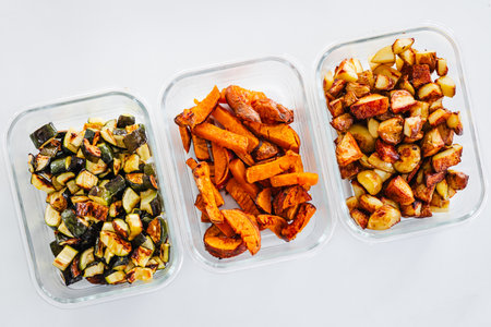 three glass containers with roasted cubed potato, sweet potato and zucchini, vegetarian meal prep...
