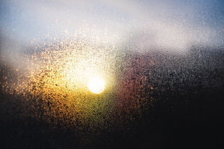 moisture droplets on a window with warm sunflare and sunrise over suburban rooftops, contrasty...
