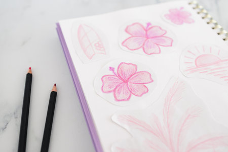 sketchpad with hand drawn pink flowers and pencils beside it on a desk, ideal for creative, artistic...