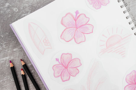sketchpad with hand drawn pink flowers and pencils beside it on a desk, ideal for creative, artistic...