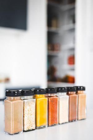 glass jars of garlic, onion, turmeric, paprika, ginger, garam masala and chinese five spice lined up on a kitchen countertop, perfect for cooking, food prep and kitchen lifestyle themesの写真素材