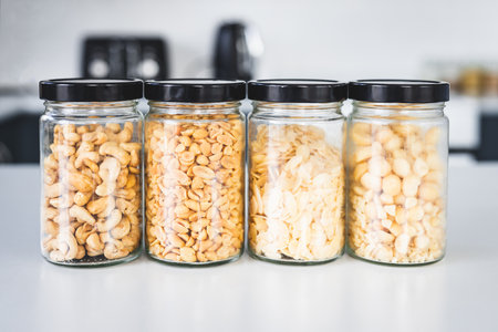 matching glass pantry jars with cashews peanuts macadamias and almond flakes on kitchen counter,...