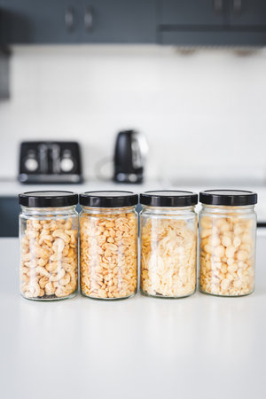 matching glass pantry jars with cashews peanuts macadamias and almond flakes on kitchen counter,...