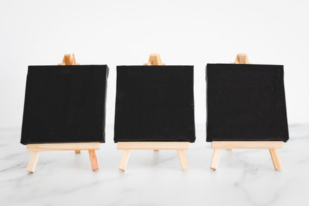 three black canvases on miniature easels on white marble desk, minimalist mockup background for...