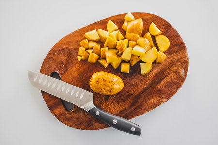 baby potatoes chopped on wooden board with knife beside them, fresh vegetable preparation for...
