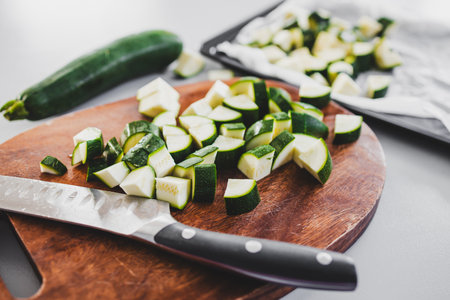 zucchini chopped on wooden board with knife beside it, fresh vegetable preparation for healthy recipesの写真素材
