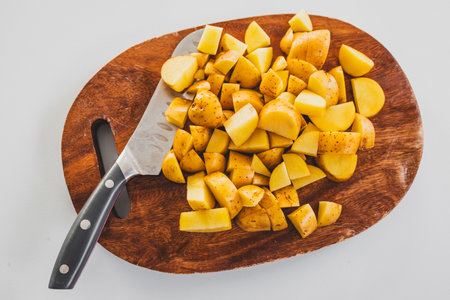baby potatoes chopped on wooden board with knife beside them, fresh vegetable preparation for...