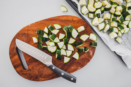 zucchini chopped on wooden board with knife beside it, fresh vegetable preparation for healthy...
