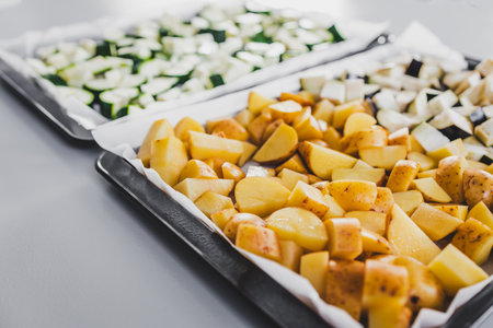 two oven trays side by side with raw chopped zucchini eggplant and baby potatoes, healthy vegetarian...