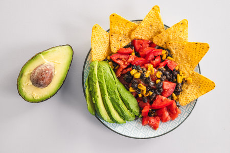 plate of healthy nachos with corn black beans tomato avocado and a few corn chips, vegetarian food...