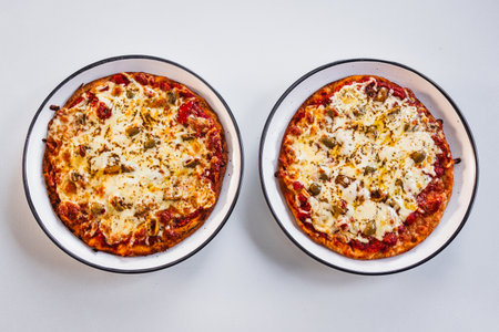 two small margherita pizzas with olives on large platesの写真素材