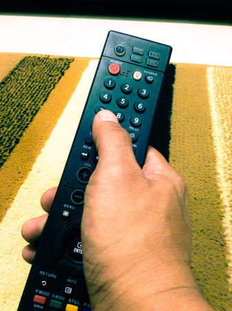 Hand holding a tv remote controlの素材