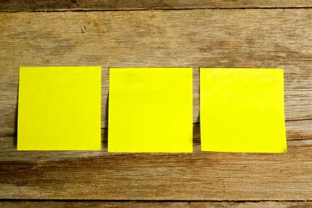 Top view of three blank yellow sticky note on wooden background with copy space.の写真素材