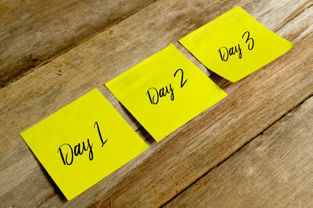Top view of yellow sticky notes written with DAY 1,DAY2,DAY3 on wooden background.Concept for blog title and header.の写真素材