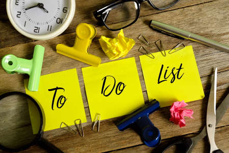 Business concept. Top view of yellow sticky notes written with TO DO LIST with pen,sunglasses,table clock,paper clip,magnifier and scissors on wooden background.の写真素材