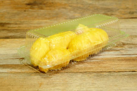 Selective focus of durian fruit inside clear plastic container on rustic wooden table. Durian is delicious tropical and king of fruit, sweet and good smell. Ripe durian has yellow gold color.の写真素材
