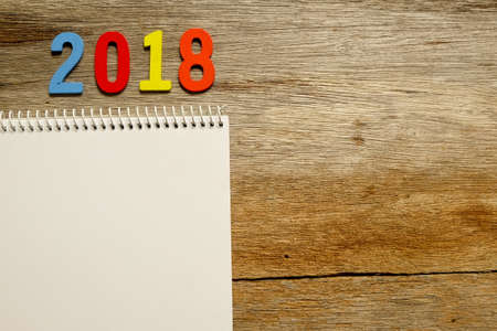 Top view of colorful wooden number 2018 and notepad with spiral on wooden background with copy...