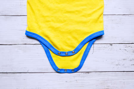 Top view of yellow and blue baby romper on white wooden background. Copy space for text or graphic.の写真素材