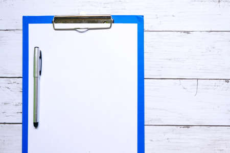 Business and finance theme. Top view of clipboard with empty white sheet and pen on wooden background. Copy space for text or logo.の写真素材
