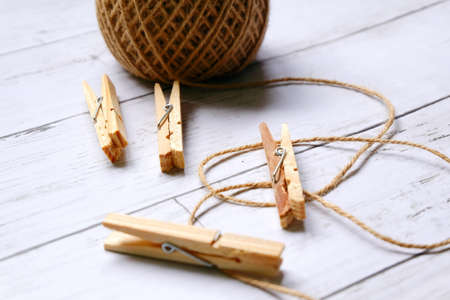 miscellaneous theme. Close up view of cloth pegs and brown rope on white wooden background.
