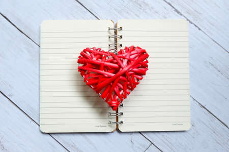 Top view of red wooden handcraft heart symbol on open book on white wooden background. Valentine's day theme.の写真素材