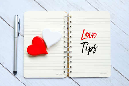 Top view of red and white wooden handcraft heart symbol on open book written with 'LOVE TIPS' on...