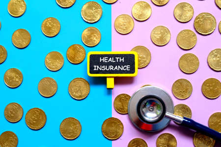Top view of gold coins,stethoscope and blackboard written with 'HEALTH INSURANCE' on blue and purple background. の写真素材