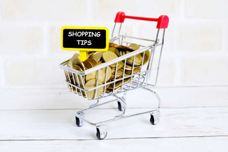 Selective focus of shopping cart or trolley with coins and yellow blackboard written with 'SHOPPING...