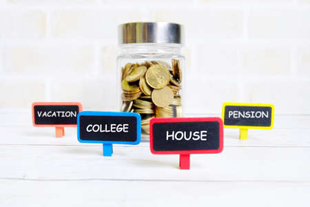 Selective focus of jar of gold coins with four blackboard written with 'VACATION','COLLEGE','HOUSE' and 'PENSION. Saving types theme.の写真素材