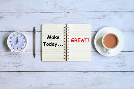 Top view of notebook written with 'MAKE TODAY GREAT!' with table clock pen and a cup of coffee on white wooden background.の写真素材