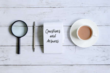 Top view of a cup of coffee,magnifying glass,pen and notepad written with 'QUESTIONS AND ANSWERS' on white wooden background.の写真素材