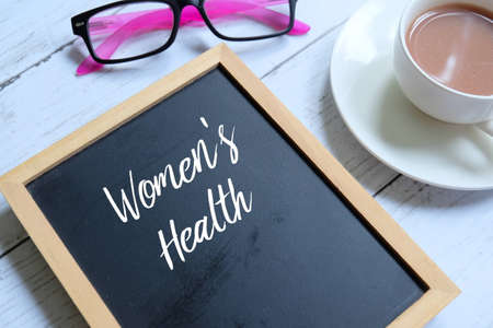 Sunglasses,a cup of coffee and blackboard written with 'WOMEN'S HEALTH' on white wooden background. Healthcare and medical theme.の写真素材