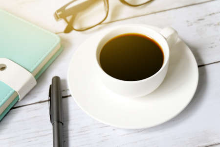 Top view and selective focus of a cup of black coffee with sunglasses, notebook and pen on white wooden background.の写真素材