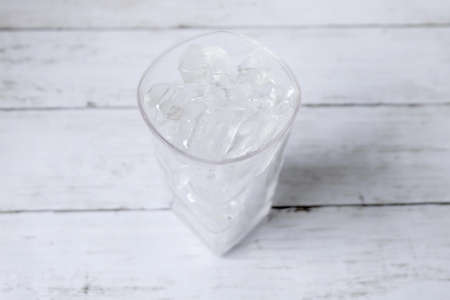 Top view of transparent glass fill with ice cube on white wooden background.の写真素材