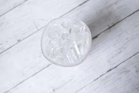 Top view of transparent glass fill with ice cube on white wooden background.の写真素材